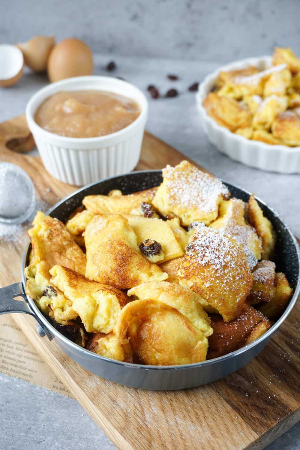 Kaiserschmarrn mit Rosinen in kleiner Pfanne, Apfelmus im Hintergrund