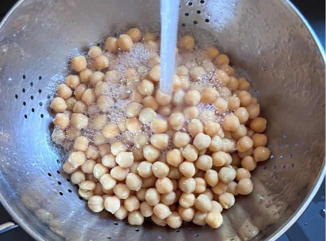 Kichererbsen sind in einem Sieb und Wasser läuft darüber
