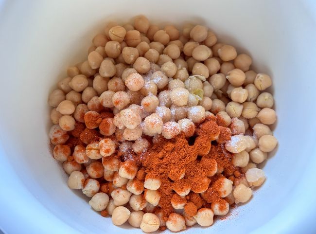 Kichererbsen mit Salz und Paprikapulver in einer weißen Schüssel