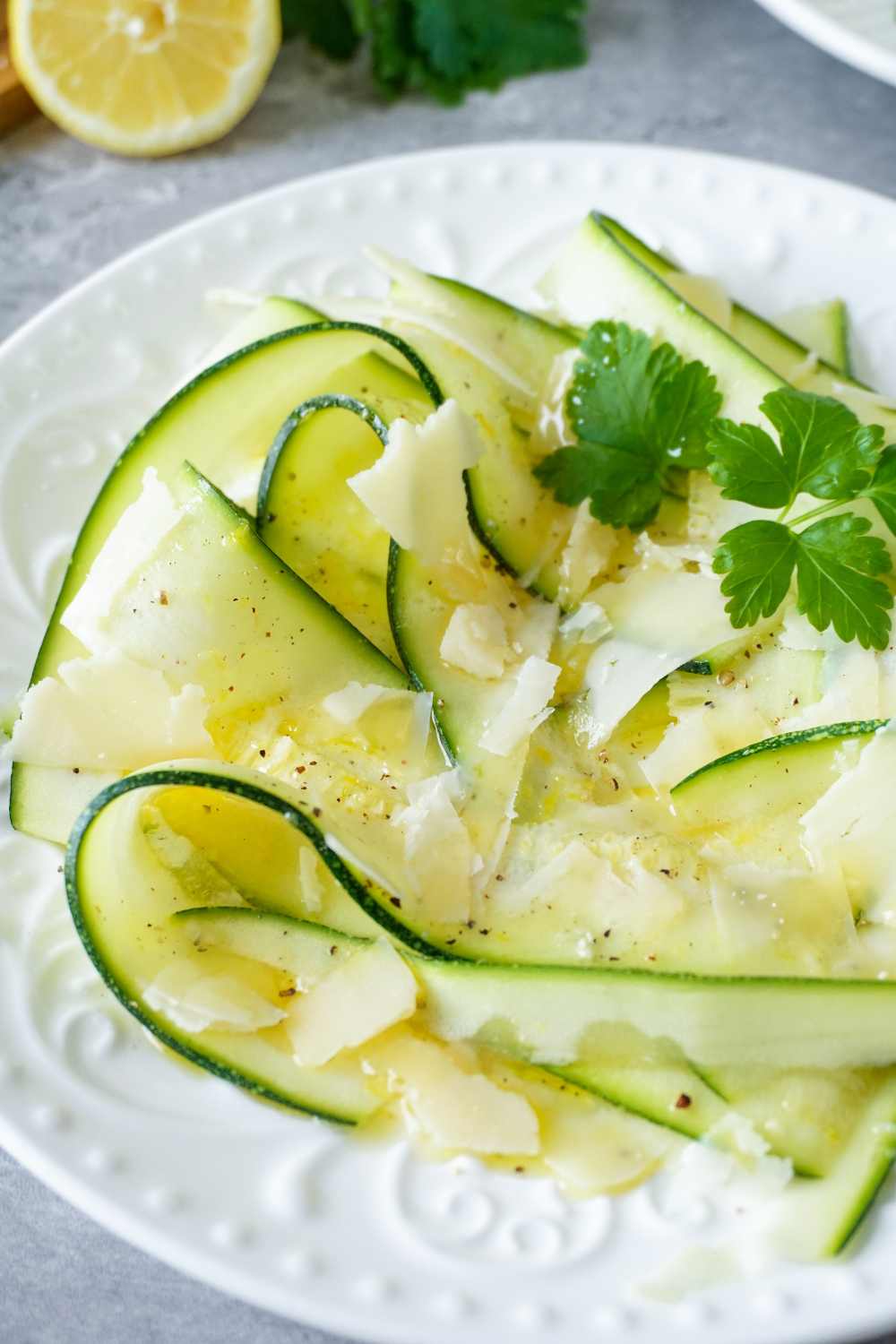 Zucchini Carpaccio Rezept weißer Teller mit Zucchinistreifen, Vinaigrette, Zitrone, Petersilie und Parmesan
